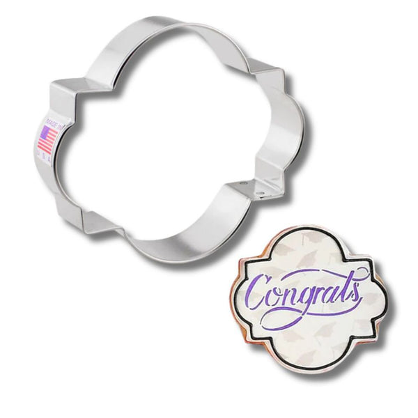 Ann Clark cookie cutter shaped like a flower, alongside a decorated cookie stating 'Congrats'.