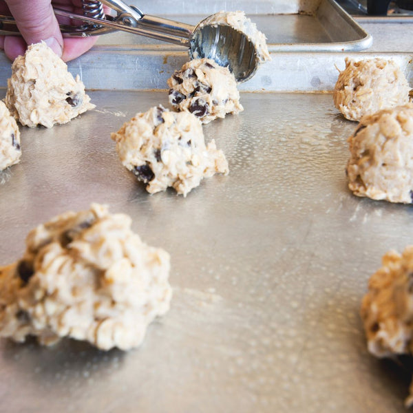 Stainless steel ice cream disher scooping cookie dough onto a baking sheet, showcasing perfect portion sizes.