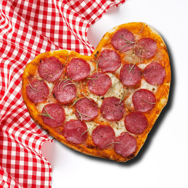 Heart-shaped pizza topped with pepperoni on a red and white checked tablecloth.