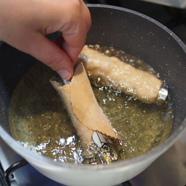 Frying cannoli tubes in hot oil, showcasing the pastry dough being wrapped around the metal forms. Crown cookware, made in Canada, 